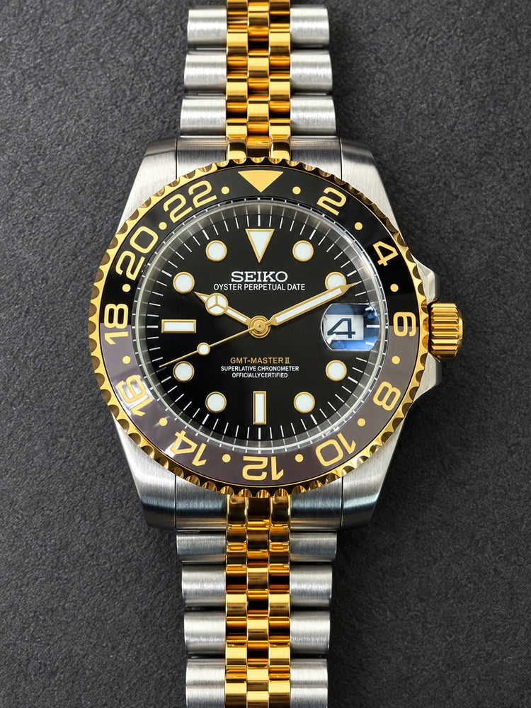 Front view of a custom two-tone Seiko 3-hand automatic watch with black dial, gold bezel with black-and-grey 24-hour insert and steel-and-gold jubilee-style bracelet