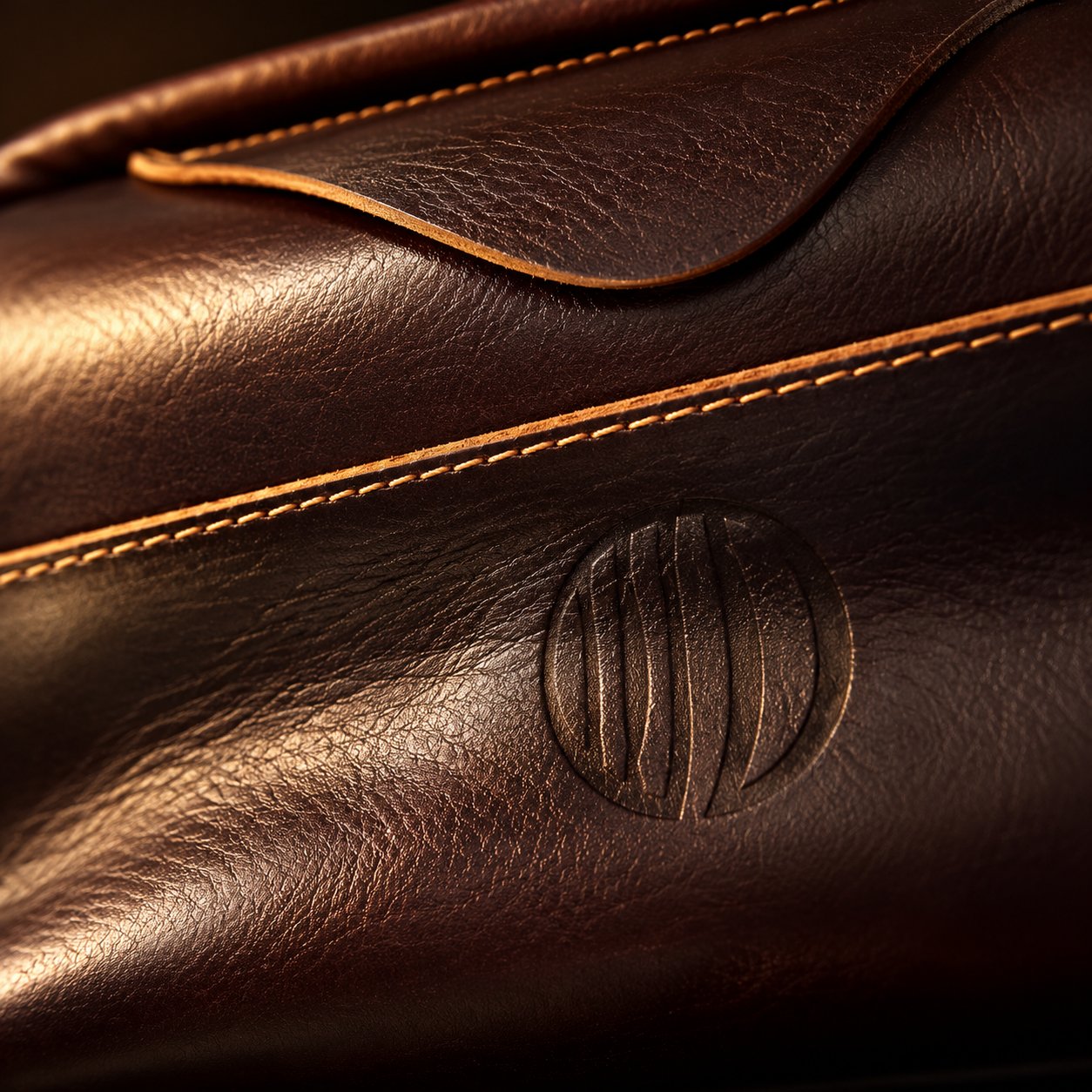 Close-up of the engraved round emblem, tan stitching and flap edge on the Vintage Coffee Leather Pouch